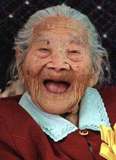 an old woman smiling and holding a banana in her hand while wearing a red sweater