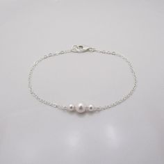 GENUINE STERLING SILVER - A GREAT KEEPSAKE This dainty pearl bracelet is made using sterling silver chain and a sterling silver lobster clasp. Two 4mm Swarovski pearls are placed on either side of a 6mm center pearl (available in your choice of 5 colors). Comes in a gift box, perfect for gift giving. SIZING - IMPORTANT: To determine bracelet size, measure around your wrist and add 1/2 inch to get your bracelet size. Cute Silver Bracelets, Minimal Silver Jewelry, Dainty Silver Jewelry, Dainty Silver Bracelet, Dainty Pearl Bracelet, Pearl Bracelet Silver, Bridesmaid Pearl Bracelet, Silver Pearl Jewelry, Silver Pearl Bracelet