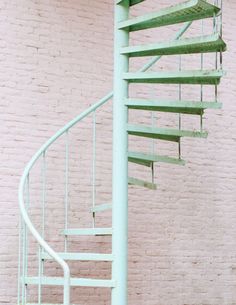 a green metal spiral staircase against a pink brick wall