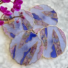 purple flowers are sitting on top of blue and gold leaf coasters, with pink stems in the background