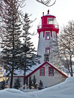 a red and white light house surrounded by trees in the middle of snow covered ground