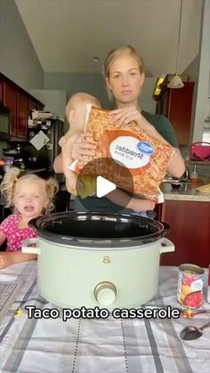 a woman holding a baby while standing in front of an crock pot