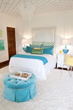 a white bedroom with blue and green accents on the bed, nightstands, and footstools