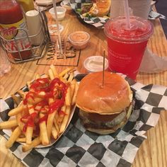 a hamburger and french fries on a checkered tablecloth with drinks in the background