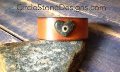 a leather bracelet with a heart on it sitting on top of a rock next to some rocks