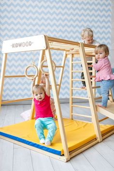 two toddlers playing on a wooden swing set with the name kiddwood written on it