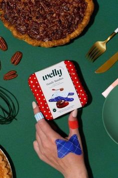 a person holding a box of jelly next to some pies and pecans on a table