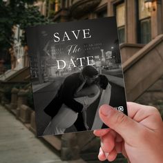 a person holding up a save the date card in front of some stairs and buildings