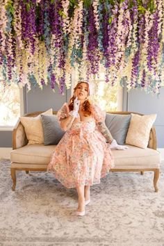 a woman sitting on a couch in front of a flower covered ceiling with purple and white flowers