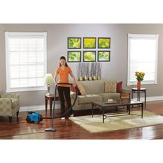 a woman in an orange shirt is cleaning a living room with a blue and black vacuum