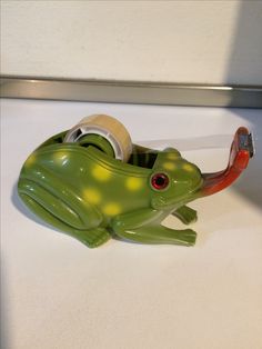 a green frog with red eyes sitting on top of a white counter next to a roll of tape