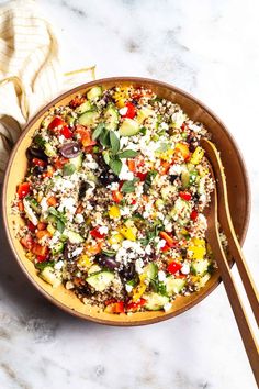 a bowl filled with salad next to two wooden spoons on top of a marble counter