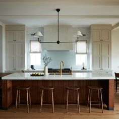 a kitchen island with three stools in front of it and two lights hanging from the ceiling