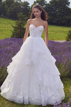 a woman in a white wedding dress standing in front of lavender flowers with trees in the background