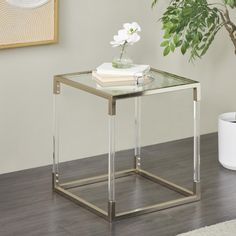 a glass and metal end table with a flower in a vase on top, next to a potted plant