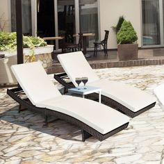 two lounge chairs sitting on top of a stone patio next to a table with a glass of wine