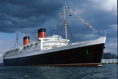 a large cruise ship in the water with flags on it's mast and some clouds