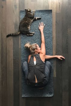 a woman laying on top of a yoga mat with a cat sitting next to her