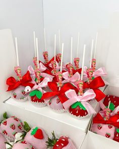 strawberry cupcakes with pink frosting and red bows are arranged on display in white boxes