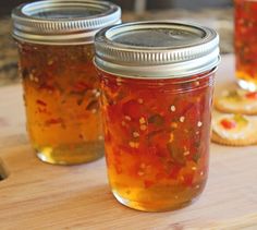 three jars filled with food sitting on top of a wooden cutting board next to cookies