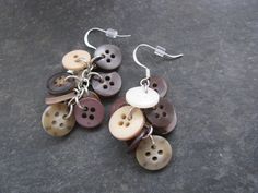 a pair of brown and white buttons are hanging from silver earwires on a stone surface