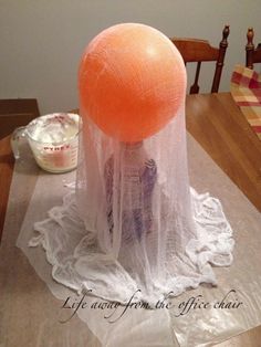 an orange ball sitting on top of a table covered in white plastic covering it's head