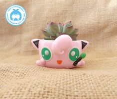 a small pink planter with green eyes on it