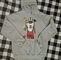 These custom-made football hoodies are great for any mom or girlfriend looking to cheer on her favorite player on game days! These hoodies are sure to keep you warm during the fall football season. Show your support in style with these mom or girlfriend-specific designs. Gray Hoodie For Sports Events In Fall, Gray Hoodie For Fall Sports Events, Fall Fan Gear Hoodie With Graphic Print, Fall Graphic Print Hoodie For Fan Gear, Team-colored Hoodie For Game Day In Fall, Football Season Fan Gear Hoodie, Team-colored Pre-shrunk Hoodie For Game Day, Football Season Fan Apparel Hoodie For Game Day, Fall Sports Fan Hoodie For Sports Events