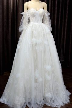 a white wedding dress on display in front of a dark background with curtains and drapes