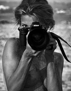 black and white photograph of a woman taking a photo with her camera on the beach