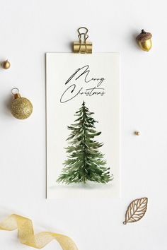 a christmas card with a watercolor pine tree on it, surrounded by gold ornaments