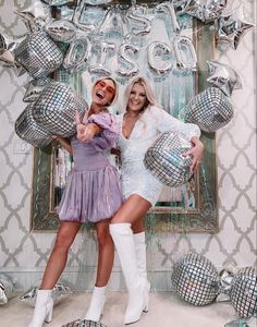 two women posing in front of balloons and disco balls