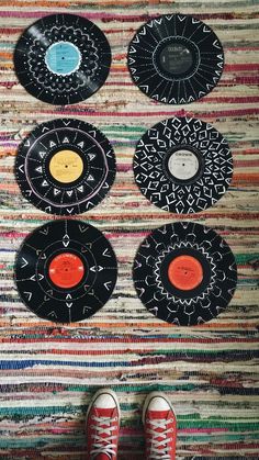 a person's feet are standing in front of four records on a rug that have been decorated with circles and arrows