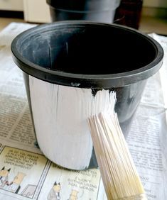 a paintbrush is sitting in front of a black pot on newspaper paper next to it