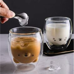 a person pouring liquid into a glass cup with a bear face on the inside and another mug in the background