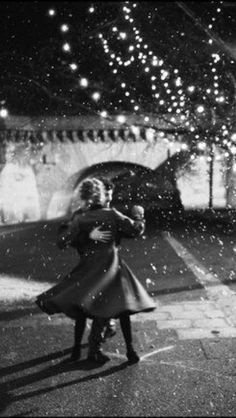 black and white photograph of two people standing in front of a bridge with lights on it