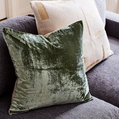 two green velvet pillows sitting on top of a gray couch