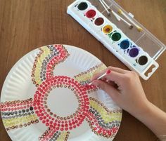 a child's hand is painting on a paper plate