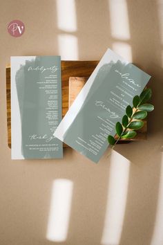 the wedding stationery is displayed on top of a wooden tray with greenery in it