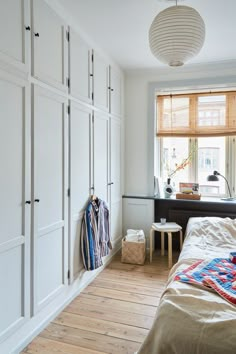 a bedroom with white closets and wooden flooring next to a bed in front of a window