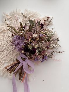 a bouquet of dried flowers is laying on a white surface next to a purple ribbon