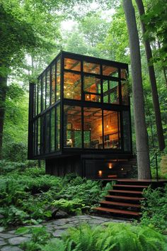 a glass cabin in the woods with stairs leading up to it's second floor