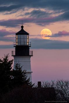 the full moon is setting behind a lighthouse