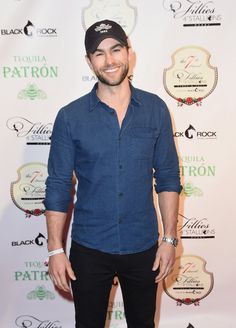 a man in a blue shirt and black pants standing on a red carpet with his hands in his pockets