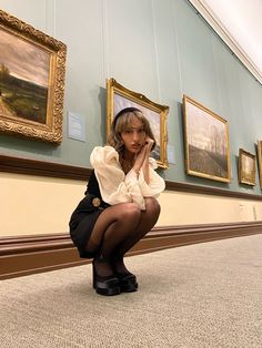 a woman sitting on the ground in front of paintings and holding her hand to her face