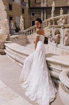 a woman in a white wedding dress standing on some steps with her back to the camera