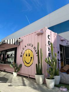 a pink shipping container with a smiley face painted on the side and cacti in front