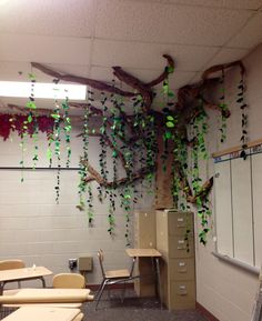 an empty classroom with desks and chairs covered in green ivy hanging from the ceiling