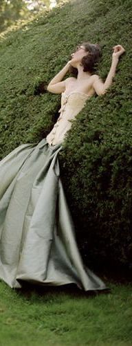 a woman in a dress leaning against a hedge