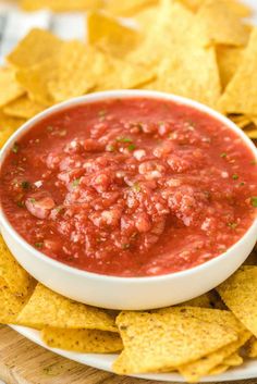 a white bowl filled with salsa surrounded by tortilla chips on a wooden platter